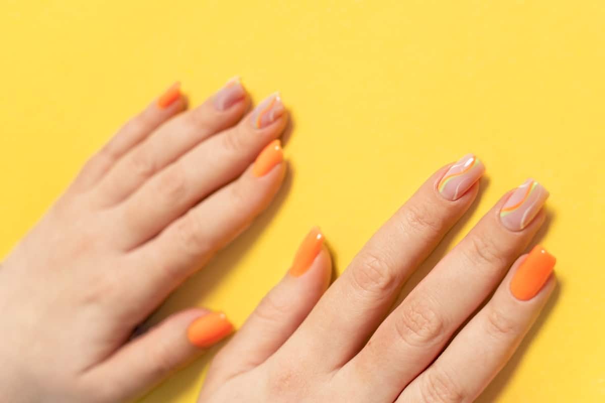 Mãos com unhas pintadas de laranja sobre superfície amarela