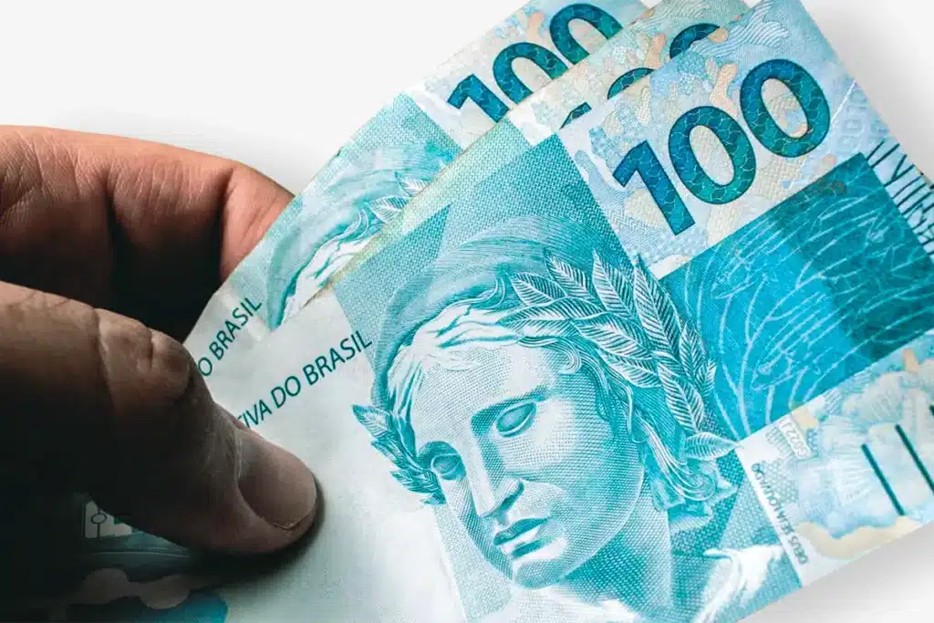Notas de 100 reais do Brasil, ilustrando uma transação financeira, usadas para explicar as dívidas cobertas pela lei.