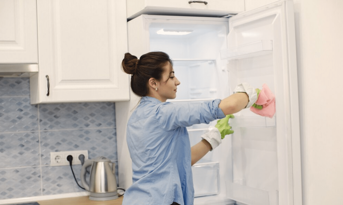 Mulher limpando a geladeira com luvas e pano, garantindo higiene e frescor