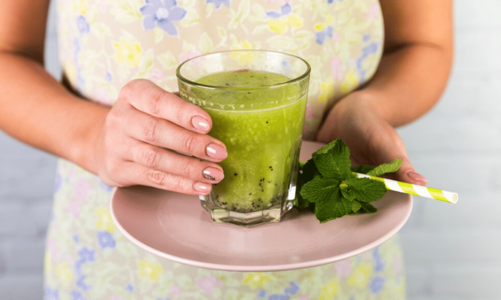 Mulher segurando um copo de suco verde com hortelã, ilustrando os benefícios para o sistema digestivo.