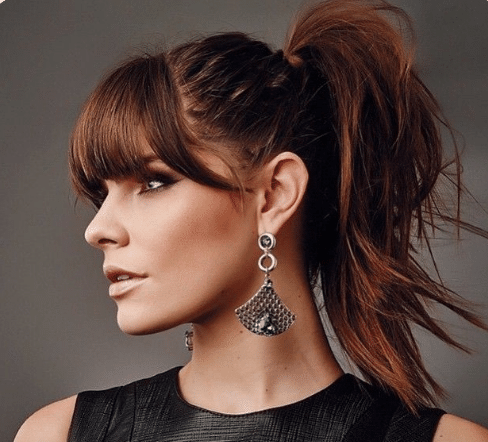 Mulher com cabelo preso em um rabo de cavalo e franja longa, usando brincos elegantes.