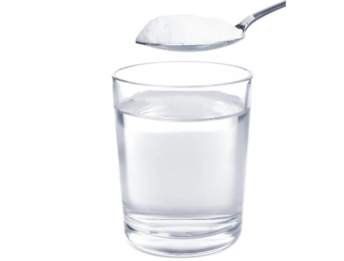 Copo de água com uma colher de bicarbonato de sódio, representando os benefícios e riscos do seu consumo.
