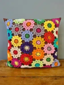 Almofada de crochê com flores coloridas sobre um fundo marrom, trazendo um toque vibrante e artesanal à decoração.