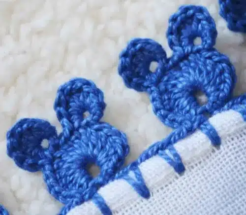 Borda de crochê azul com detalhes em formato de flores.