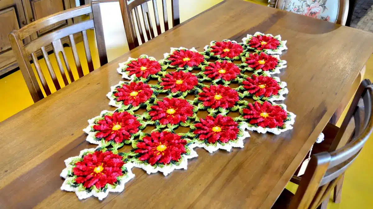 Caminho de mesa de crochê com flores vermelhas e verdes sobre uma mesa de madeira.