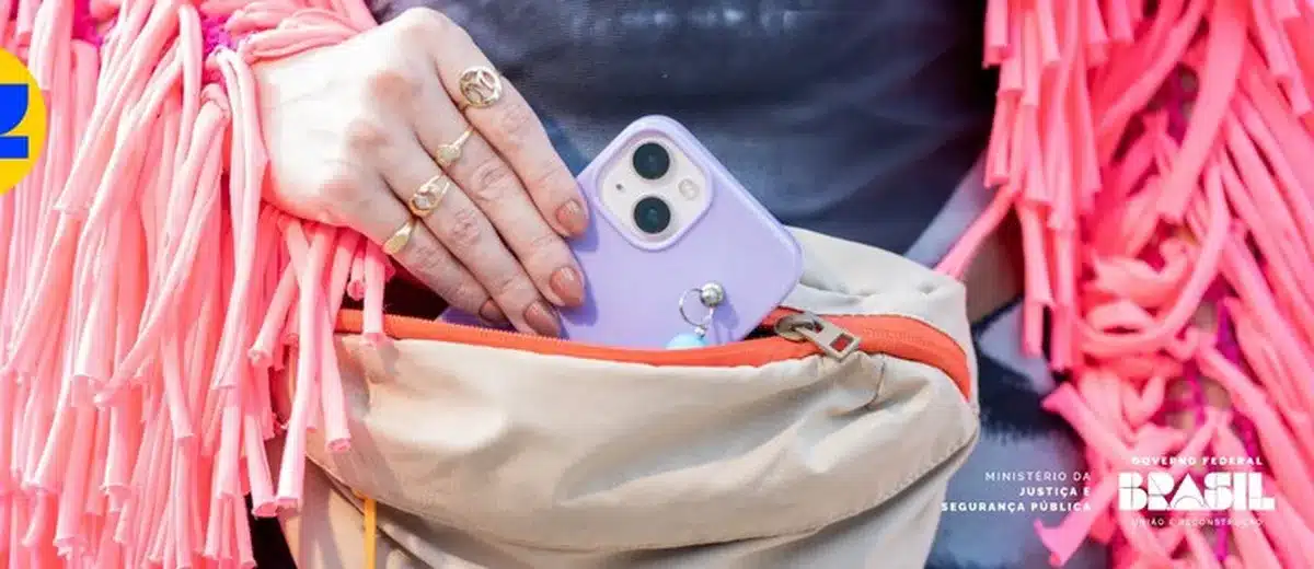 Mão segurando um celular roxo ao colocá-lo dentro de uma pochete, simbolizando segurança no Carnaval.