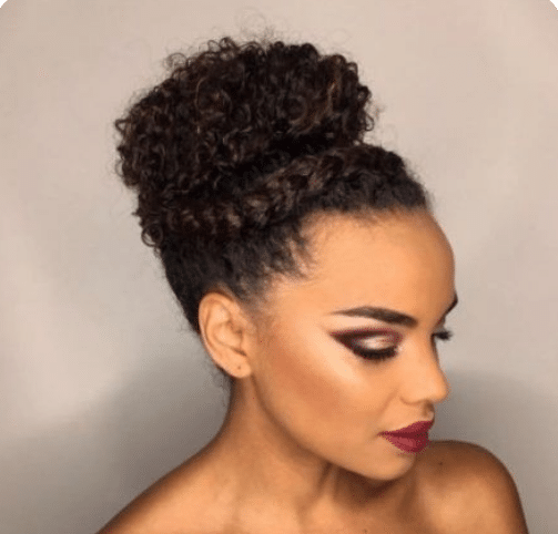 Mulher com coque alto e cabelo cacheado, com maquiagem suave e batom vinho.