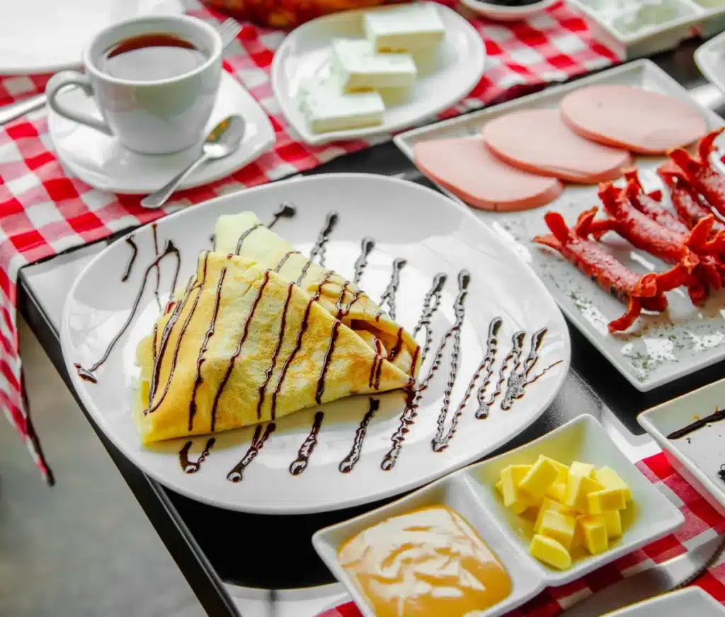 Crepes doces com calda de chocolate servidos em um café da manhã completo.