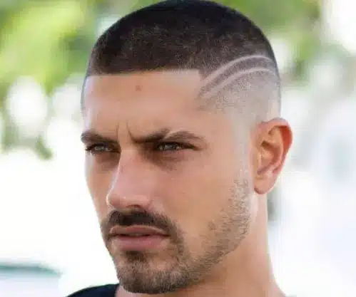 Homem com corte de cabelo buzz cut geométrico e expressão séria.