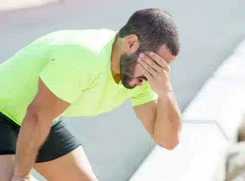 Homem exausto após exercício físico, segurando a cabeça e demonstrando fadiga, um dos sintomas do hipotireoidismo.