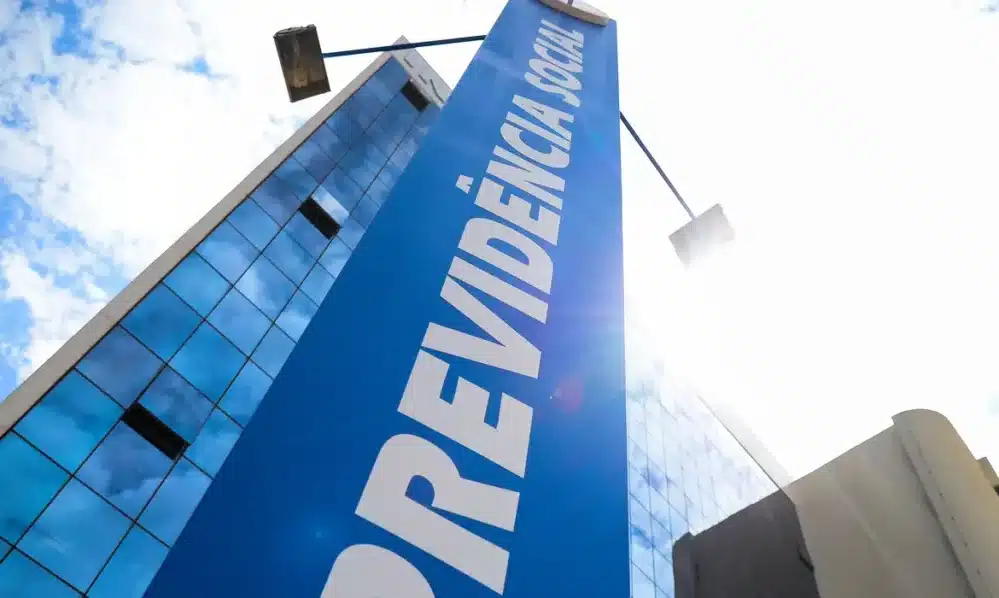 Fachada de prédio do INSS com placa azul indicando Previdência Social sob céu azul e ensolarado.