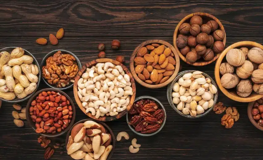 Variedade de oleaginosas como castanhas, nozes, amêndoas e avelãs dispostas em tigelas de madeira.