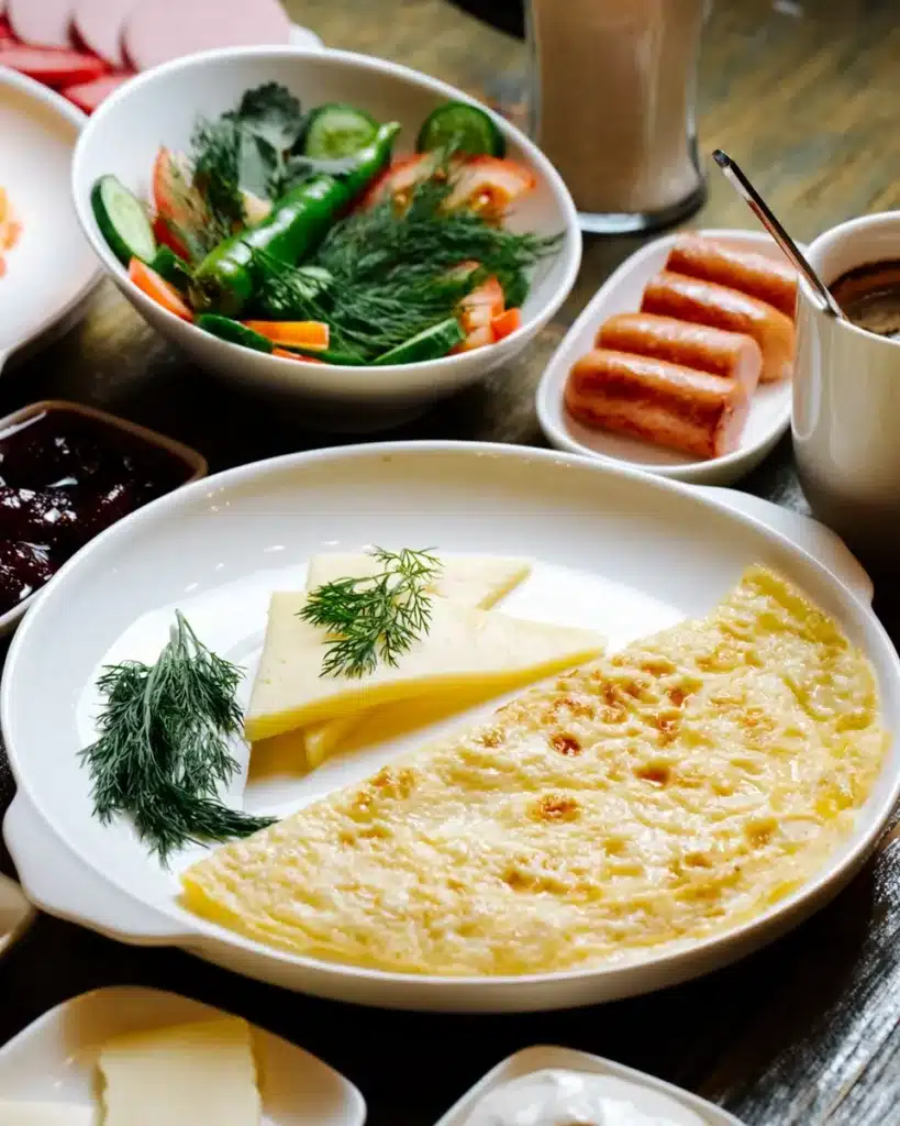 Omelete dourada servida com queijo, ervas frescas e acompanhamentos variados