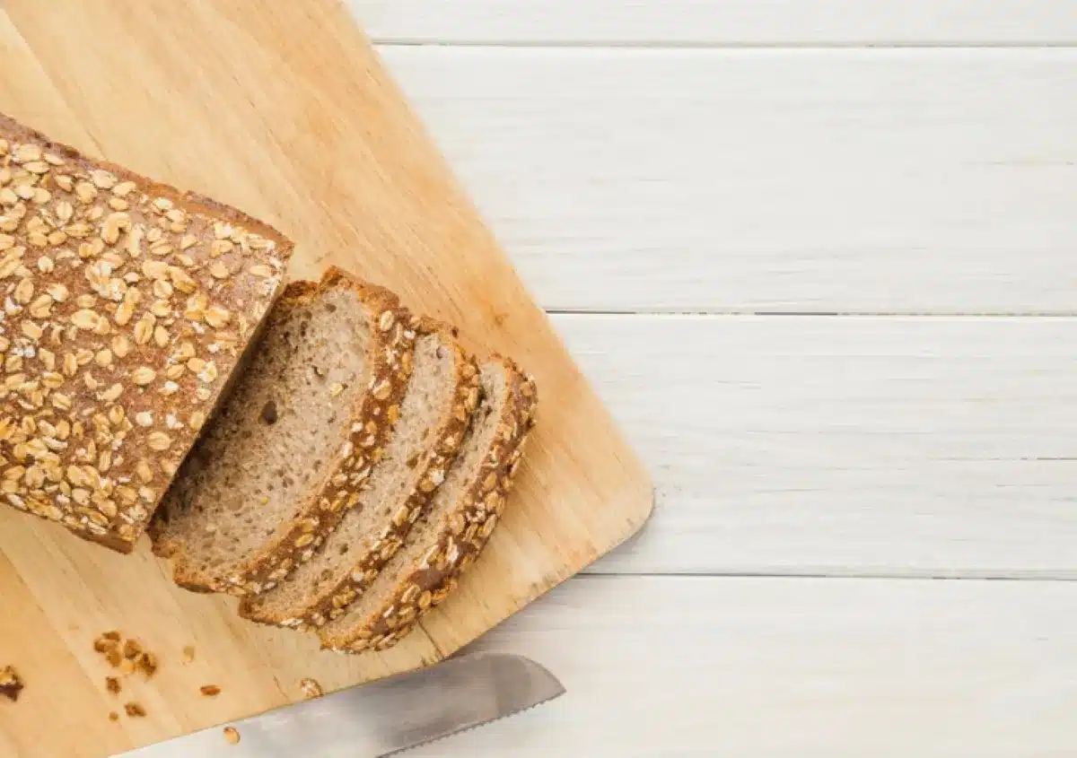 Pão de aveia fatiado sobre uma tábua de madeira, acompanhado de uma faca.