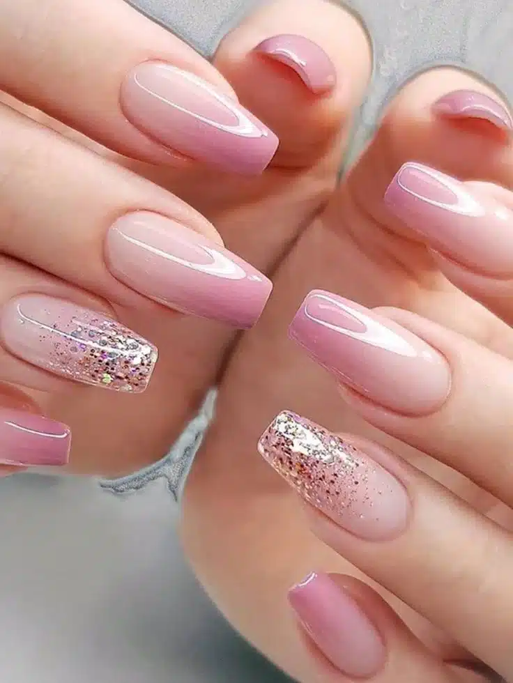 Unhas decoradas em tons de rosa com brilho, seguindo as tendências de 2025