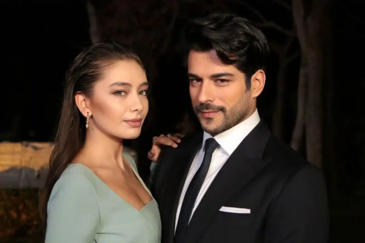 Casal de uma série turca, vestidos elegantemente, posando para uma foto promocional.