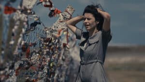 Personagem principal de O Segredo do Templo em cena dramática, segurando o cabelo em frente a uma cerca, simbolizando tensão e mistério.