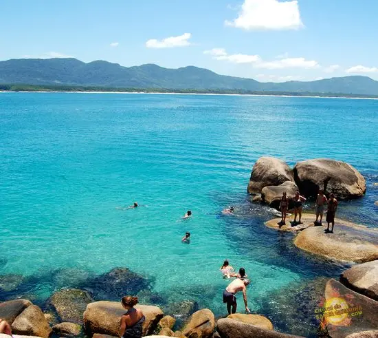 Florianópolis: paraíso natural com águas cristalinas "Pessoas aproveitando o mar cristalino e as pedras de Florianópolis, com uma paisagem deslumbrante ao fundo.