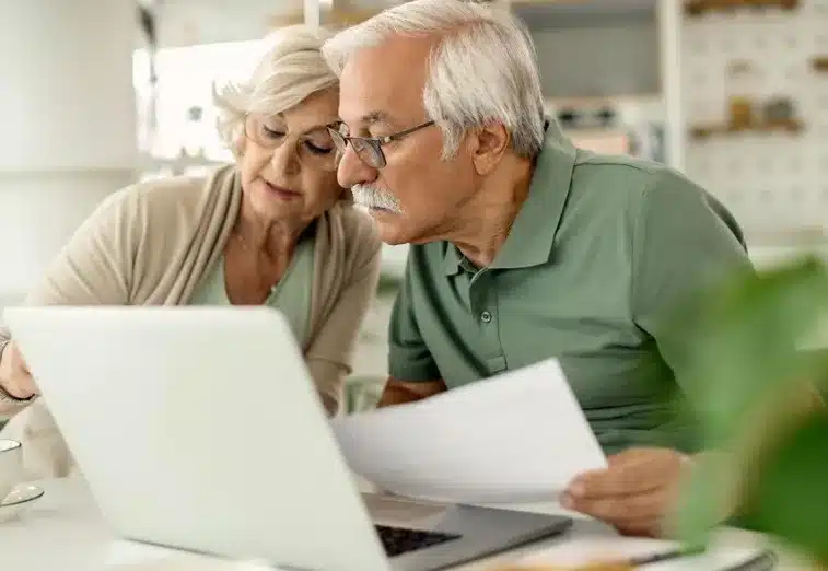 Casal de idosos analisando documentos e utilizando um caderno, representando a proteção legal contra o endividamento.