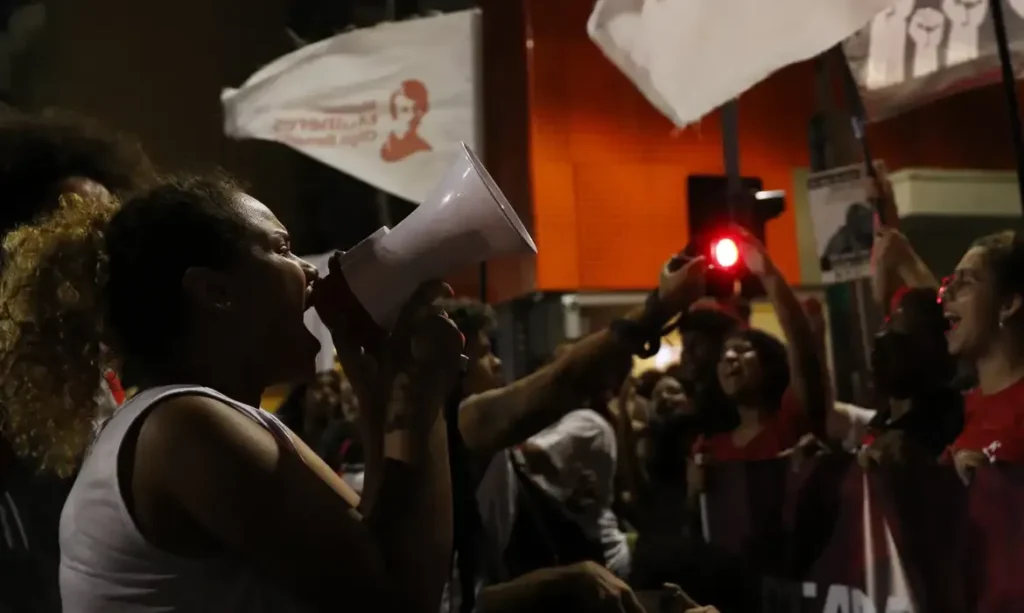 Mulher gritando ao megafone durante uma manifestação, representando a luta por direitos e voz ativa.