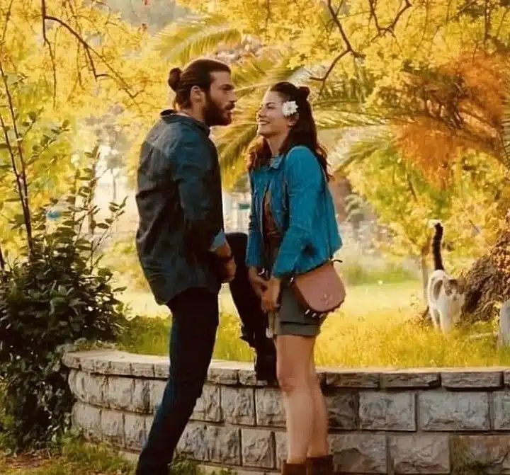 "Uma cena romântica da série 'A Sonhadora', mostrando um casal rindo e compartilhando um momento em um parque ensolarado cercado pela natureza.