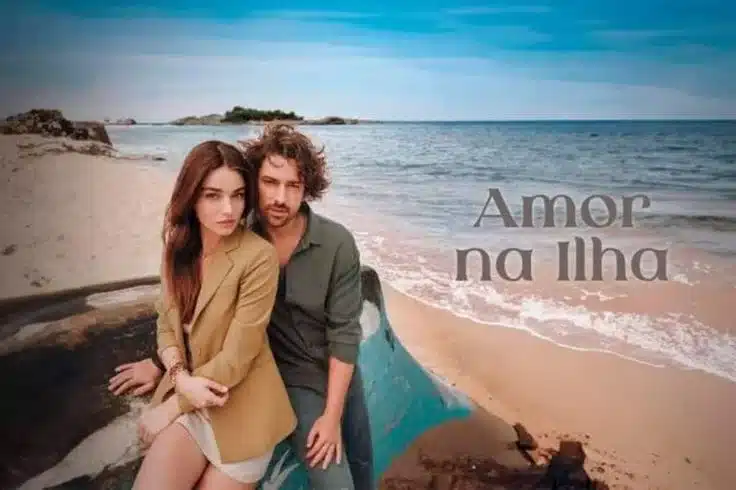 O casal principal da série 'Amor na Ilha' sentados juntos em uma praia, mostrando seu vínculo emocional com o oceano ao fundo.