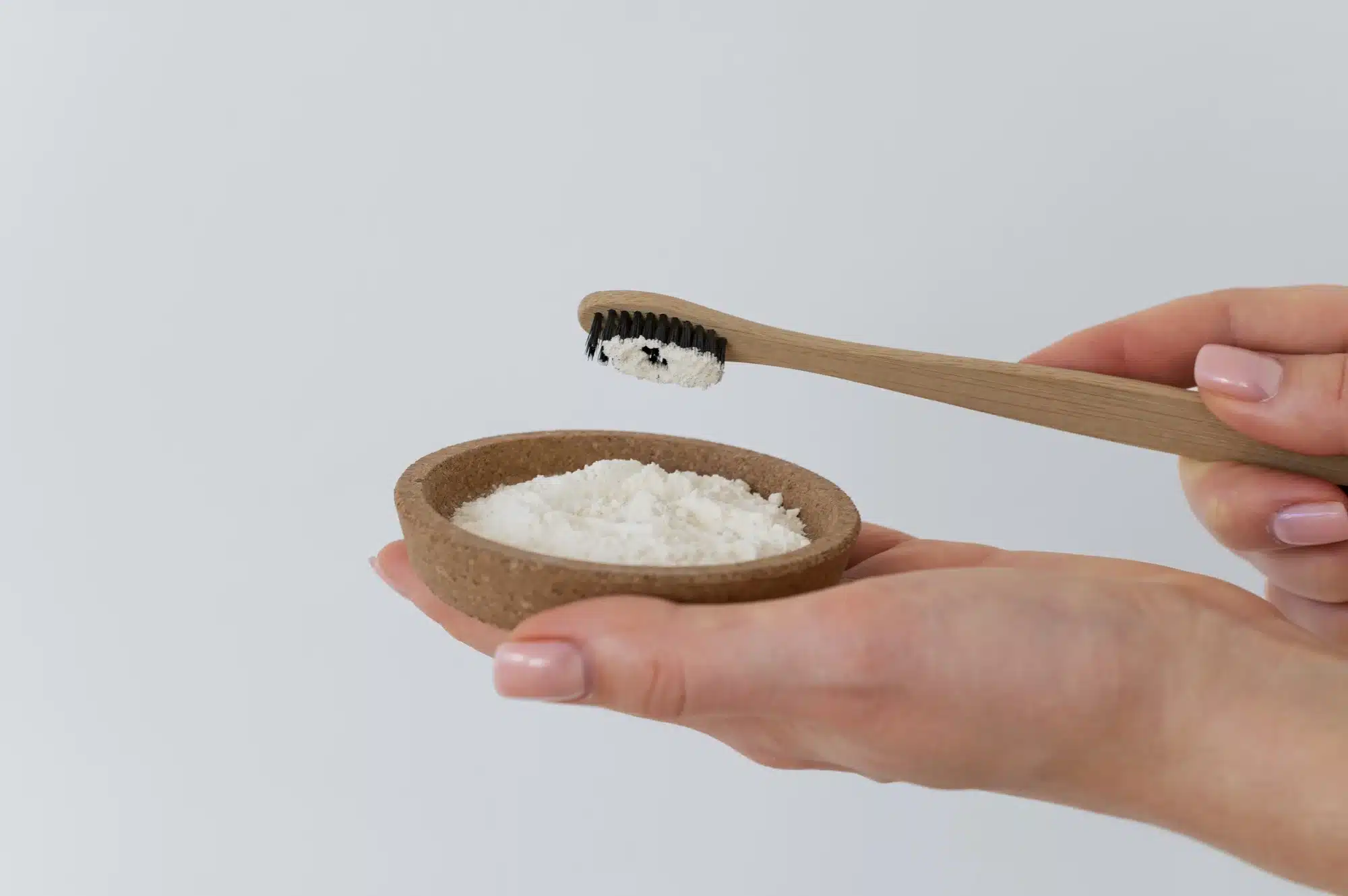 Pessoa segurando uma tigela de bicarbonato de sódio e uma escova de dentes