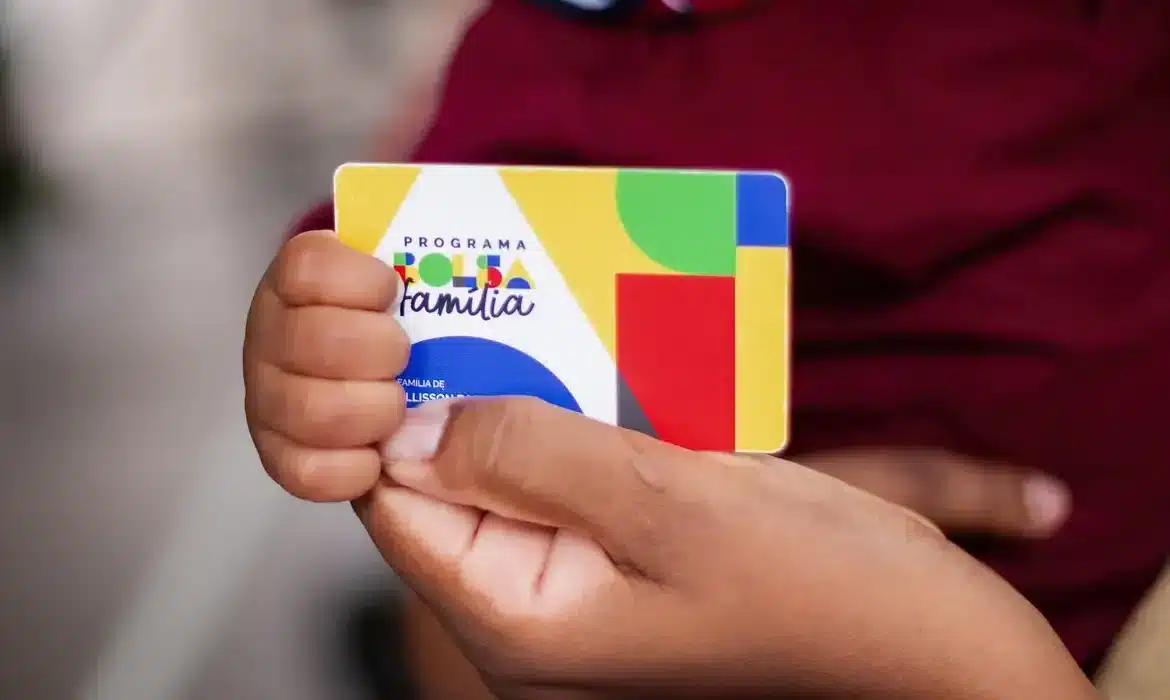 Pessoa segurando cartão do Programa Bolsa Família, representando os benefícios sociais no Brasil.