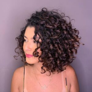 Corte bob desfiado em cabelo cacheado, com volume e definição, ideal para um visual moderno e estiloso.