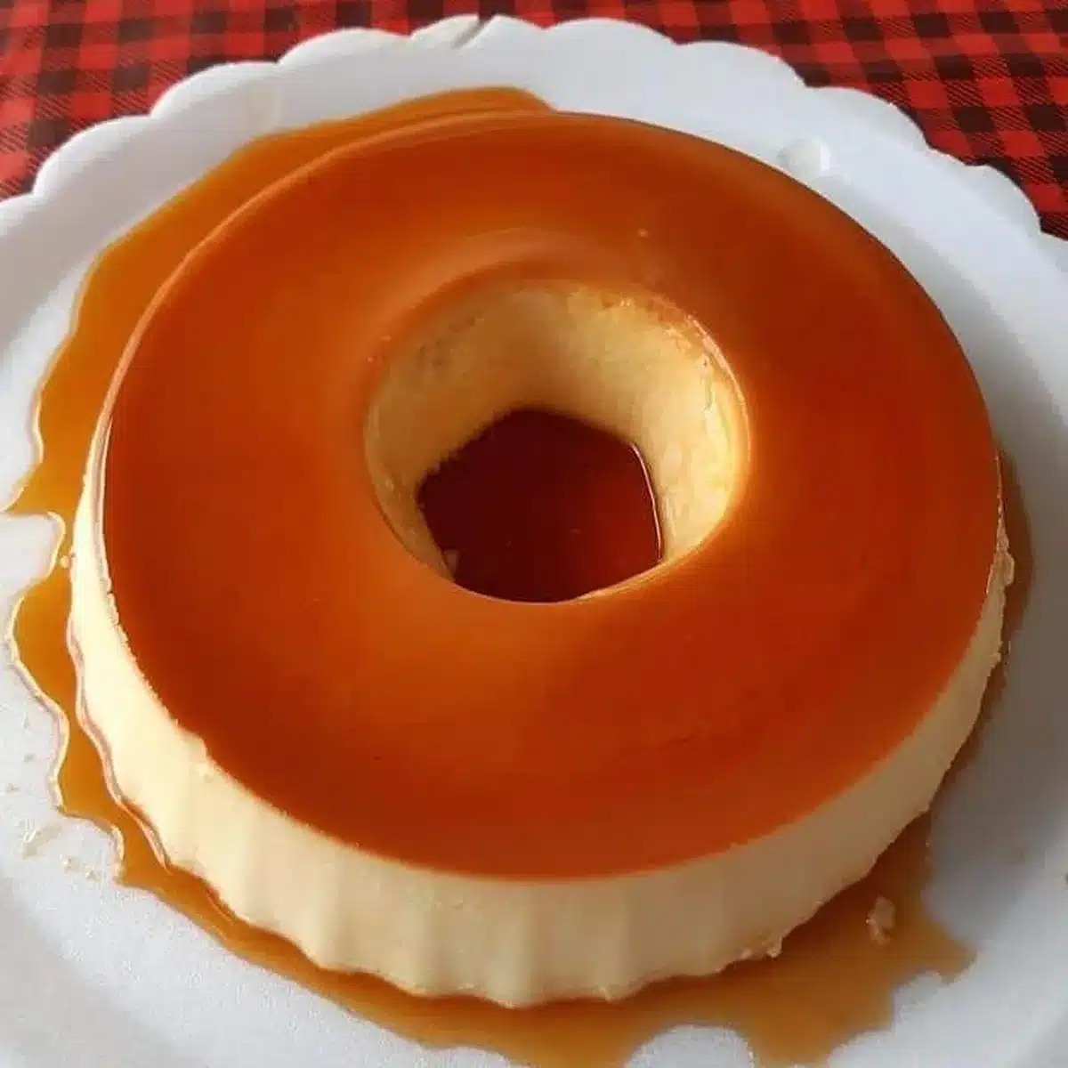 Pudim com calda caramelizada brilhante servida em prato branco.