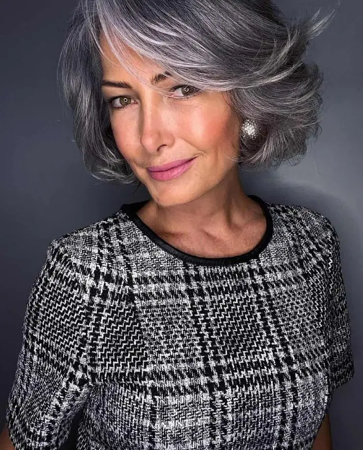 Mulher com cabelo cinza prateado e corte moderno, exalando um visual ousado e sofisticado, com a tonalidade de cabelo representando a tendência de cinza prateado para o inverno.
