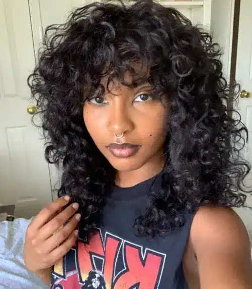 Mulher com corte shaggy moderno, cabelo cacheado e franja.