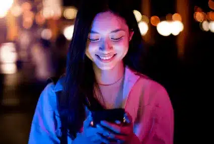  Mulher sorrindo enquanto olha para o celular à noite com iluminação suave.