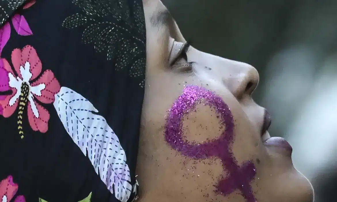 Mulher com símbolo feminino brilhante pintado no rosto, representando empoderamento.