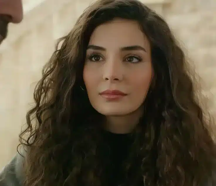 Imagem da protagonista Reyyan da novela turca 'Hercai: Amor e Vingança', com cabelo cacheado e expressando emoção.