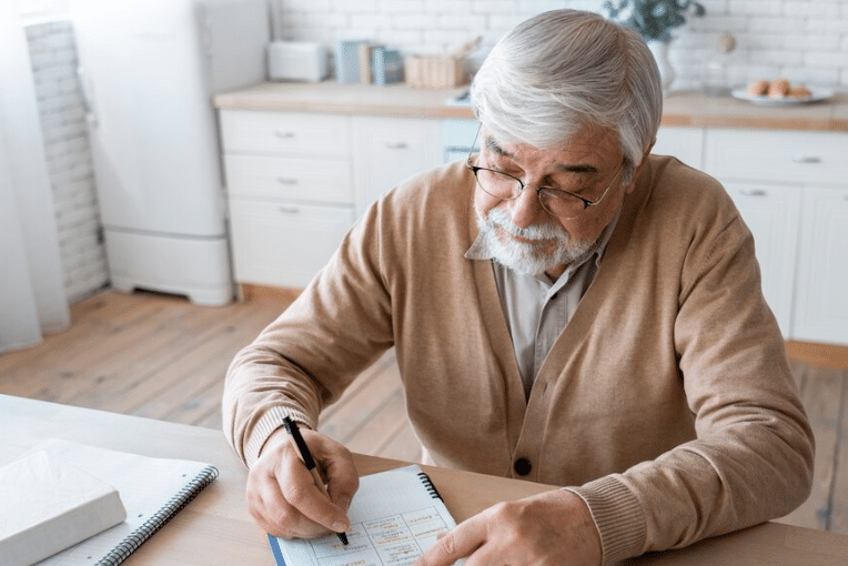 Imagem de idoso escrevendo em um caderno, simbolizando a organização financeira para se livrar de dívidas.