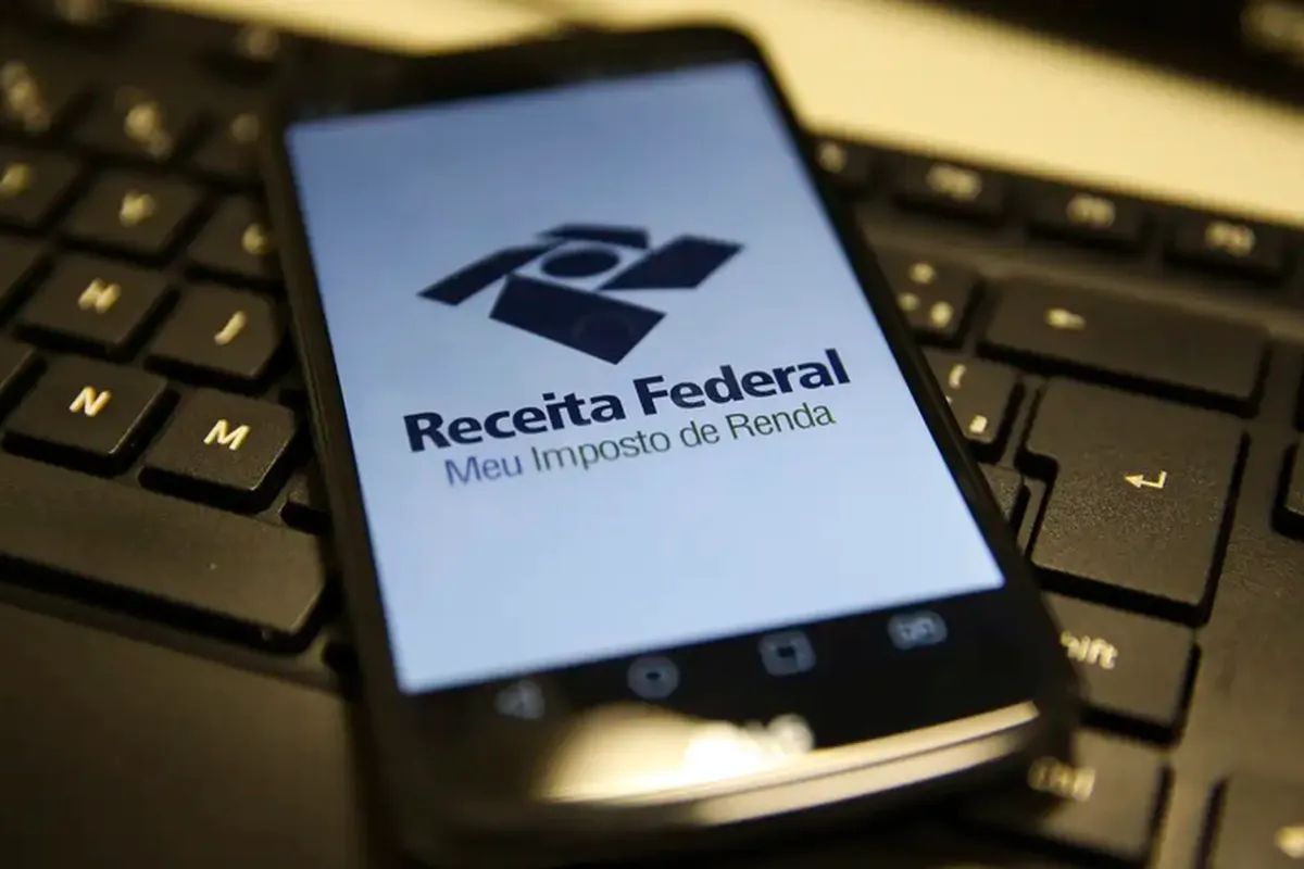 Aplicativo da Receita Federal aberto em um smartphone sobre um teclado de computador, representando o acesso à declaração do Imposto de Renda 2025.