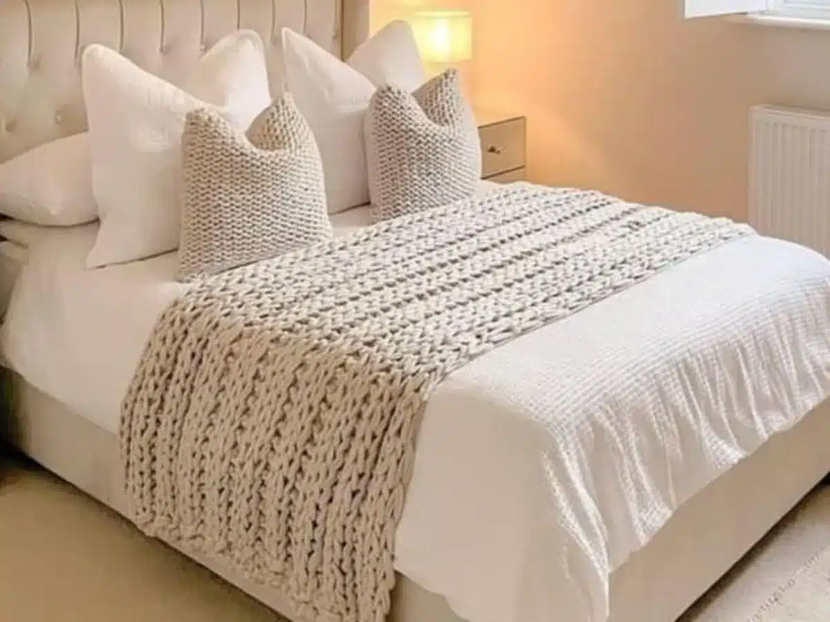 Cama elegante com peseira de crochê e almofadas combinando em tons neutros.
