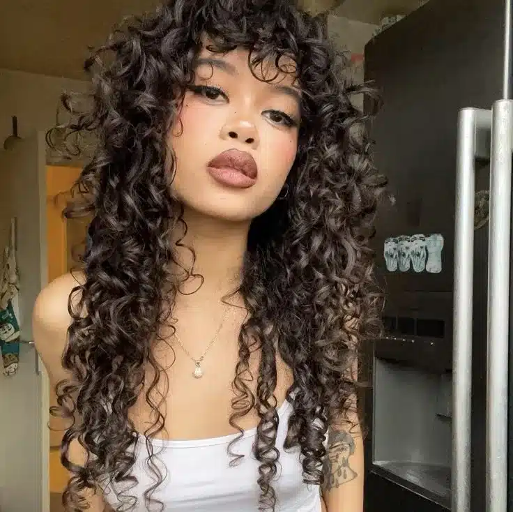 Mulher com cabelo curly e franja, estilo shaggy bob moderno e volumoso.