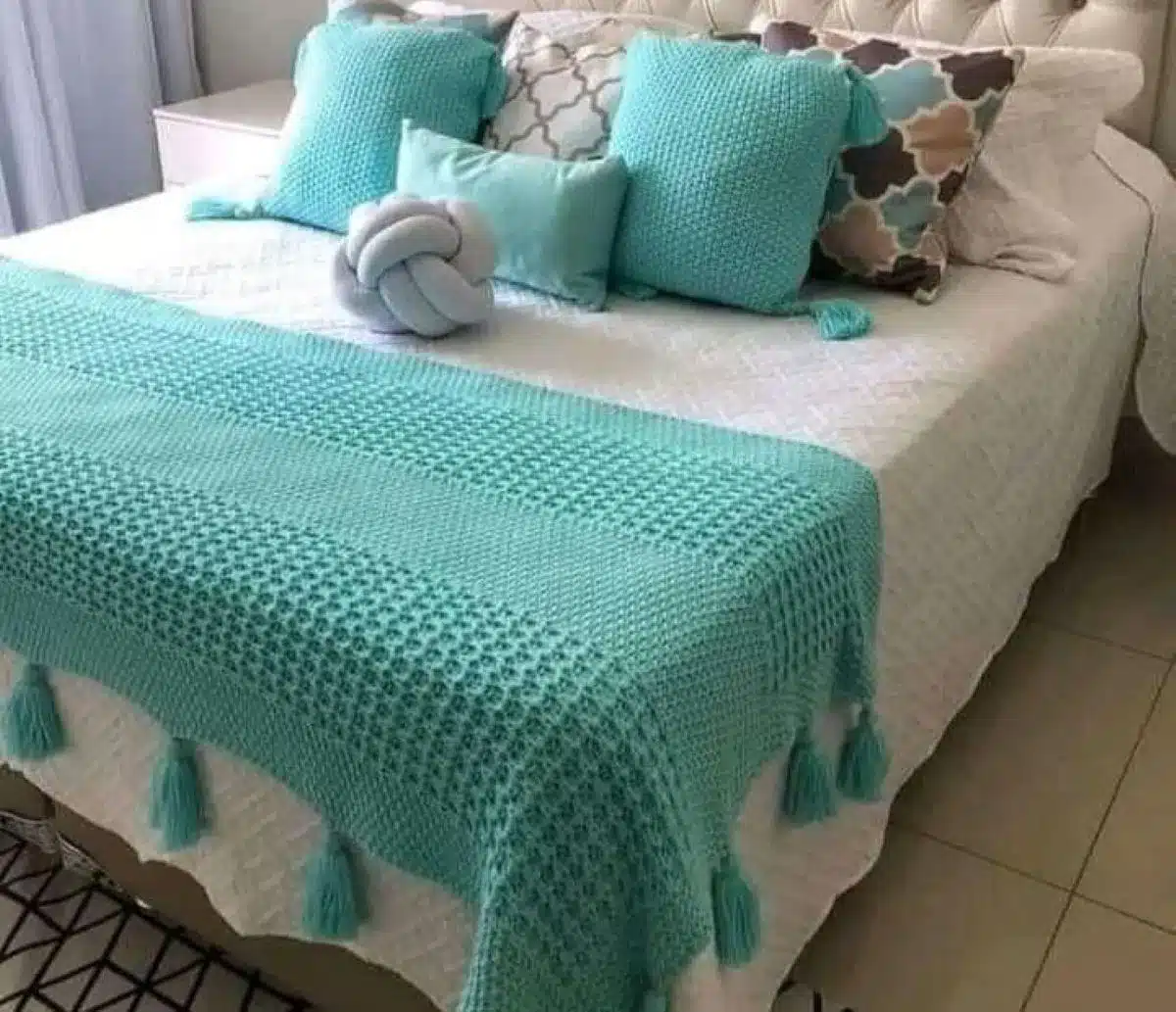 Cama decorada com peseira de crochê azul e almofadas combinando, criando um ambiente aconchegante e moderno.