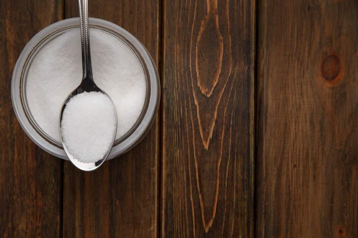 Pote de produto em pó branco com colher sobre superfície de madeira.