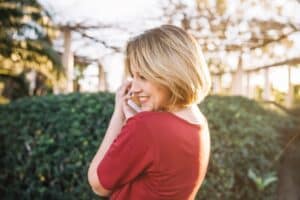 Mulher de cabelo curto loiro sorrindo ao telefone em um dia ensolarado.