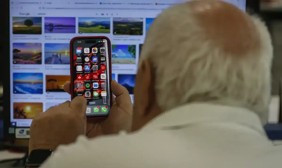 Idoso segurando um iPhone com diversos aplicativos na tela, incluindo o WhatsApp.
