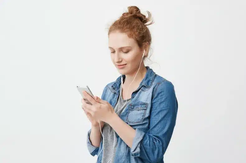 Pessoa utilizando o WhatsApp com fones de ouvido e celular na mão.