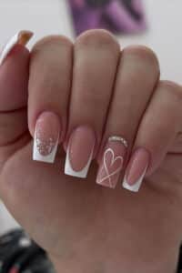 Unhas com alongamento de porcelana em formato quadrado com francesinha branca e decoração delicada com glitter e coração.