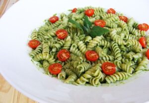 Macarrão com molho pesto, tomates cereja e folhas de manjericão, prato fresco e saboroso.