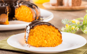 Bolo de cenoura fofinho com calda de chocolate crocante, servido em prato com porção.