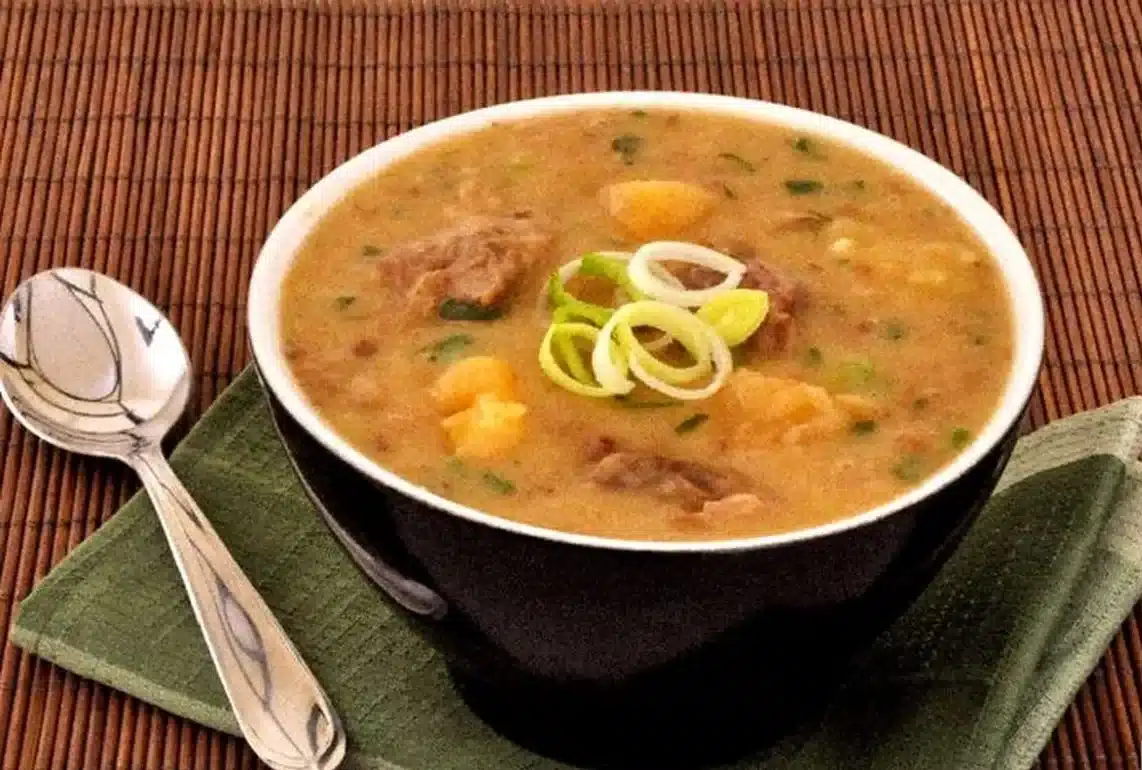 Caldo de vaca atolada com pedaços de carne e batata, servido em tigela preta.