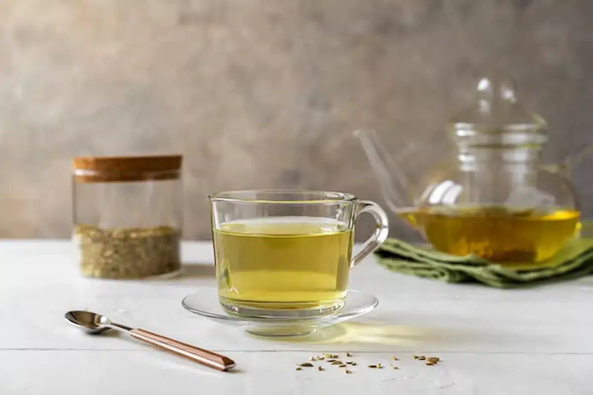  Xícara de chá de erva-doce sobre mesa clara com sementes e bule ao fundo