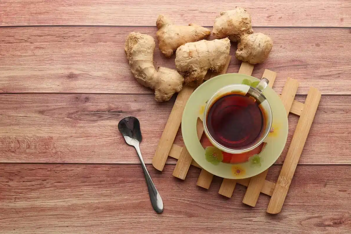 Vista superior de xícara de chá de gengibre com raiz fresca ao fundo sobre mesa de madeira